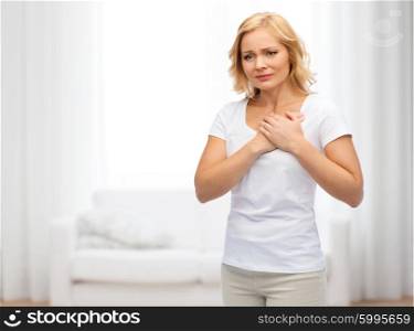 people, healthcare, heart disease and problem concept - unhappy woman suffering from heartache over living room background