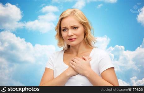 people, healthcare, heart disease and problem concept - unhappy woman suffering from heartache over blue sky and clouds background