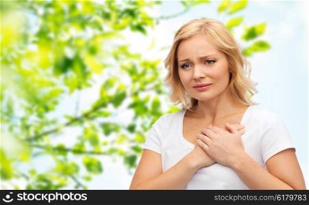 people, healthcare, heart disease and problem concept - unhappy woman suffering from heartache over green natural background