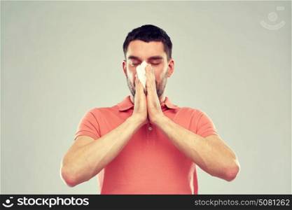 people, healthcare, rhinitis, cold and allergy concept - sick man with paper napkin blowing nose over gray background. sick man with paper napkin blowing nose