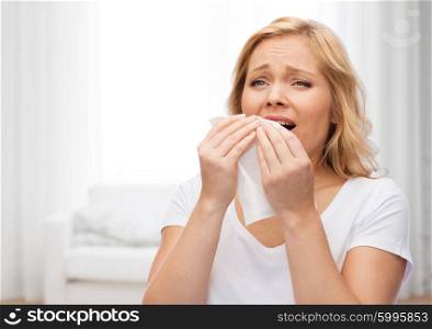 people, healthcare, rhinitis, cold and allergy concept - unhappy woman with paper napkin sneezing over living room background