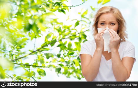 people, healthcare, rhinitis, cold and allergy concept - unhappy woman with paper napkin blowing nose over natural background