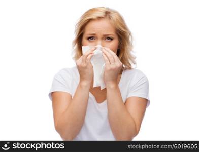 people, healthcare, rhinitis, cold and allergy concept - unhappy woman with paper napkin blowing nose