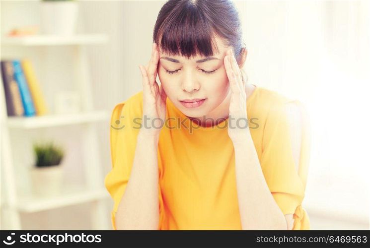 people, healthcare, stress and problem concept - unhappy asian young woman suffering from headache at home. tired asian woman suffering from headache at home