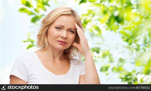 people, healthcare, stress and problem concept - unhappy woman suffering from headache over green natural background