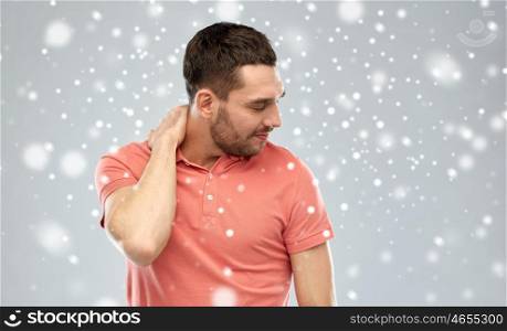 people, healthcare, winter, christmas and problem concept - unhappy man suffering from neck pain over snow on gray background