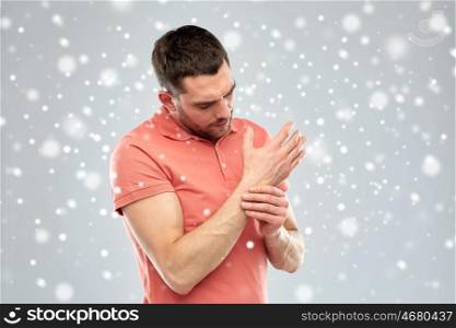 people, healthcare, winter, christmas and problem concept - unhappy man suffering from pain in hand over snow on gray background