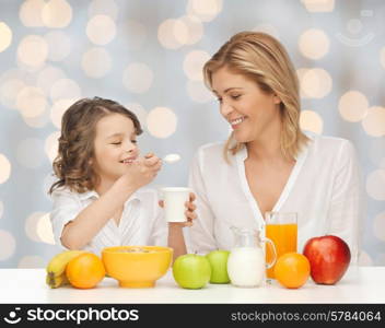 people, healthy lifestyle, family and food concept - happy mother and daughter eating healthy breakfast over holidays lights background