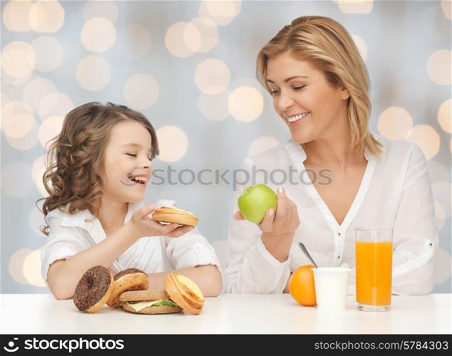 people, healthy lifestyle, family and food concept - happy mother and daughter eating healthy breakfast over holidays lights background