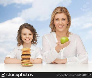 people, healthy lifestyle, family and unhealthy food concept - happy mother and daughter eating different food over blue sky background