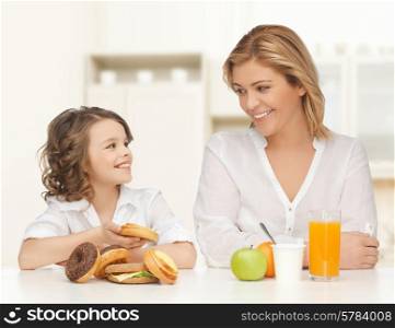 people, healthy lifestyle, family and unhealthy food concept - happy mother and daughter eating different food over home kitchen background