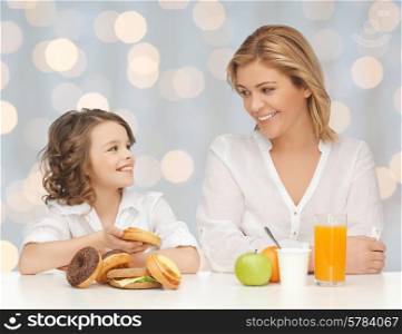people, healthy lifestyle, family and unhealthy food concept - happy mother and daughter eating different food over holidays lights background