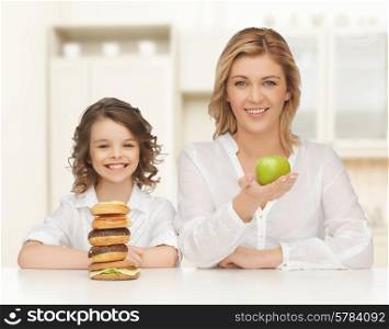 people, healthy lifestyle, family and unhealthy food concept - happy mother and daughter eating different food over home kitchen background