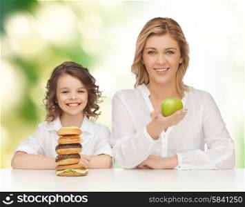 people, healthy lifestyle, family and unhealthy food concept - happy mother and daughter eating different food over green background