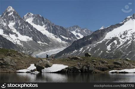 People hiking and doing trekking by a lake in the mountains with glacier on the background