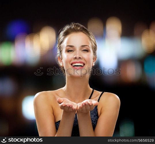 people, holidays, advertisement and luxury concept - laughing woman in evening dress holding something imaginary over night lights background
