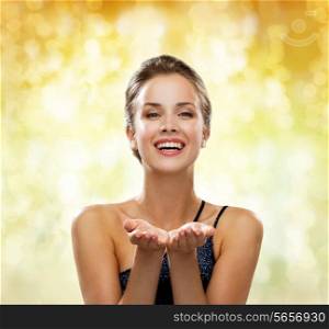 people, holidays, advertisement and luxury concept - laughing woman in evening dress holding something imaginary over yellow lights background