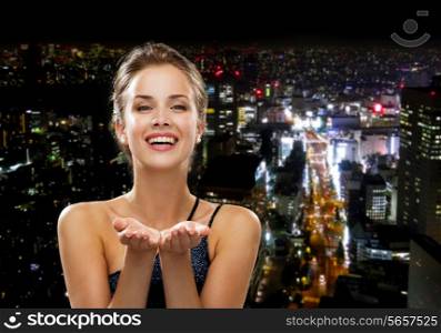 people, holidays, advertisement and luxury concept - laughing woman in evening dress holding something imaginary over night city background