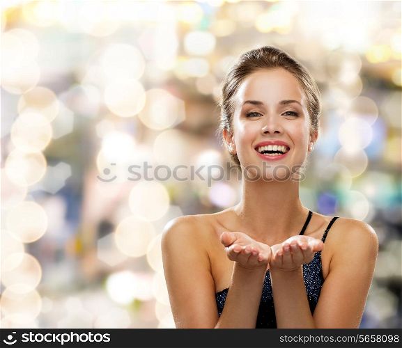 people, holidays, advertisement and luxury concept - laughing woman in evening dress holding something imaginary over lights background