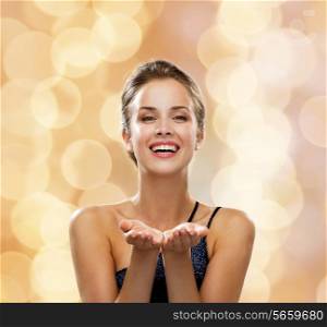 people, holidays, advertisement and luxury concept - laughing woman in evening dress holding something imaginary over beige lights background