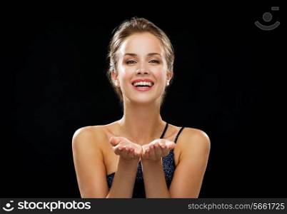 people, holidays, advertisement and luxury concept - laughing woman in evening dress holding something imaginary over black background