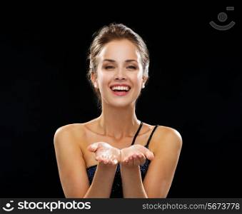 people, holidays, advertisement and luxury concept - laughing woman in evening dress holding something imaginary over black background