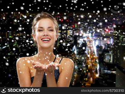 people, holidays, advertisement and luxury concept - laughing woman in evening dress holding something imaginary over snowy night city background