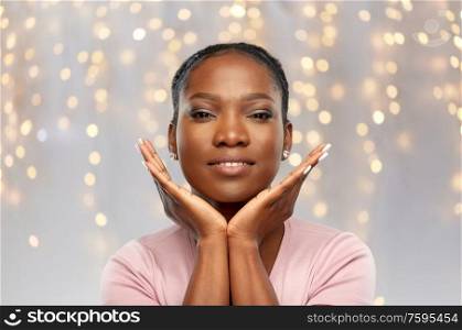 people, holidays and beauty concept - portrait of happy smiling african american young woman over festive lights background. happy african american woman over lights