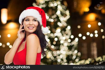 people, holidays and celebration concept - beautiful sexy woman in santa hat calling on cellphone over christmas tree background. beautiful woman calling on cellphone at christmas