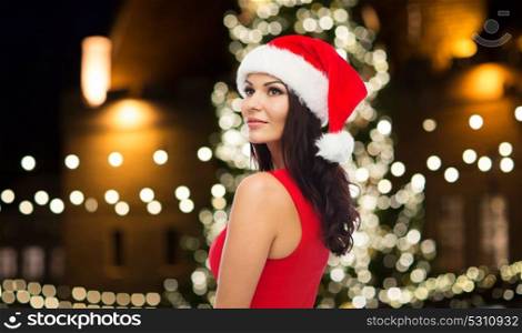 people, holidays and celebration concept - beautiful sexy woman in santa hat and red dress over christmas tree background. beautiful sexy woman in santa hat at christmas