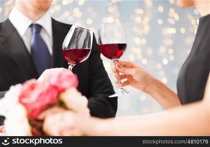 people, holidays and celebration concept - close up of couple clinking red wine glasses over lights background