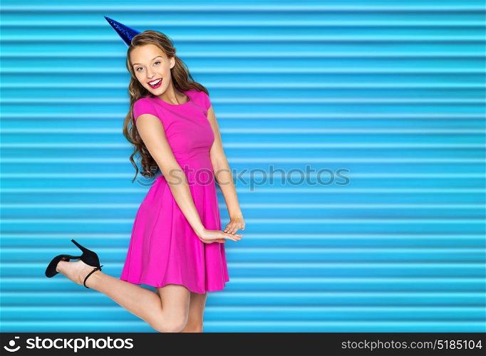 people, holidays and celebration concept - happy young woman or teen girl in pink dress and party cap over blue ribbed background. happy young woman or teen girl in party cap