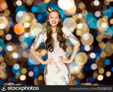 people, holidays and celebration concept - happy young woman or teen girl in party dress and princess crown over festive lights background. happy young woman in crown over festive lights