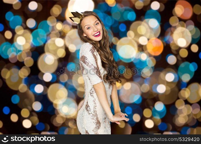 people, holidays and celebration concept - happy young woman or teen girl in party dress and princess crown over festive lights background. happy young woman in crown over festive lights