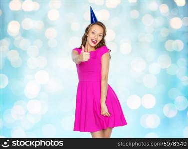people, holidays and celebration concept - happy young woman or teen girl in pink dress and party cap over blue holidays lights background