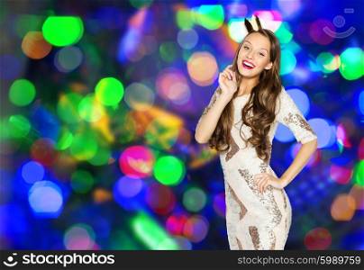 people, holidays and celebration concept - happy young woman or teen girl in party dress and princess crown over lights background