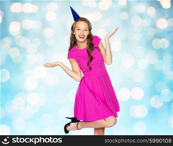 people, holidays and celebration concept - happy young woman or teen girl in pink dress and party cap over blue lights background