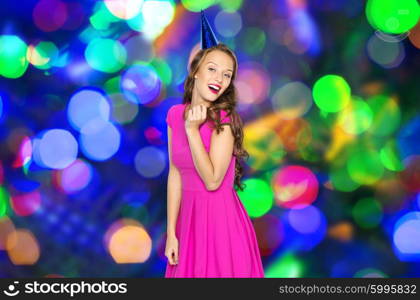 people, holidays and celebration concept - happy young woman or teen girl in pink dress and party cap over disco lights background