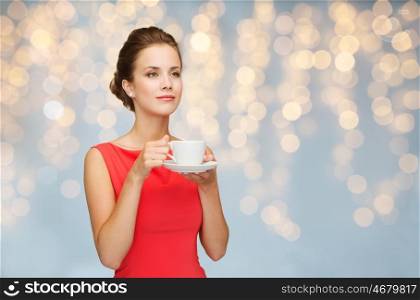 people, holidays and drinks concept - smiling woman in red dress with cup of coffee over lights background