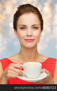 people, holidays and drinks concept - smiling woman in red dress with cup of coffee over lights background
