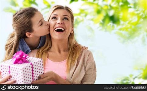 people, holidays and family concept - daughter kissing happy mother and giving her birthday present over green natural background. daughter kissing mother and giving her present