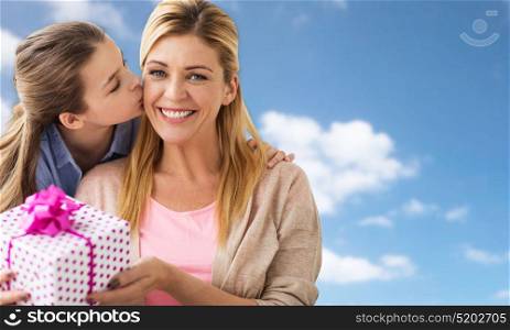 people, holidays and family concept - happy girl giving birthday present to mother over blue sky and clouds background. girl giving birthday present to mother over sky