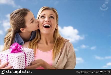 people, holidays and family concept - happy girl giving birthday present to mother over blue sky and clouds background. girl giving birthday present to mother over sky