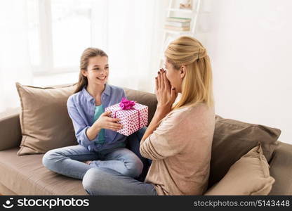 people, holidays and family concept - happy girl giving birthday present to mother at home. girl giving birthday present to mother at home