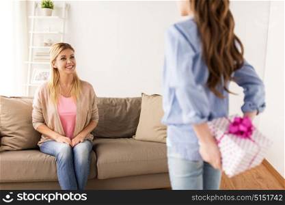 people, holidays and family concept - happy girl giving birthday present to mother at home. girl giving birthday present to mother at home