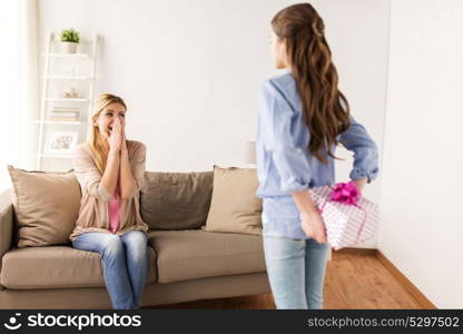 people, holidays and family concept - happy girl giving birthday present to mother at home. girl giving birthday present to mother at home