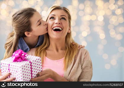 people, holidays and family concept - happy girl giving birthday present to mother over lights background. girl giving birthday present to mother over lights