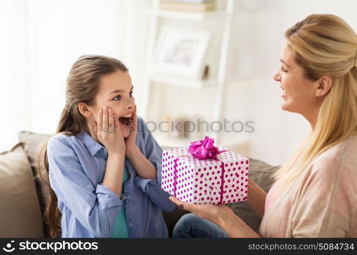 people, holidays and family concept - happy girl receiving birthday present from mother at home. mother giving birthday present to girl at home. mother giving birthday present to girl at home