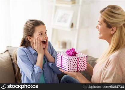 people, holidays and family concept - happy girl receiving birthday present from mother at home. mother giving birthday present to girl at home. mother giving birthday present to girl at home