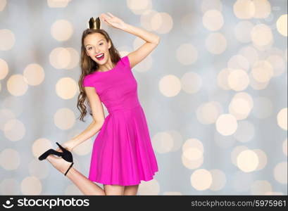 people, holidays and fashion concept - happy young woman or teen girl in pink dress and princess crown over lights background